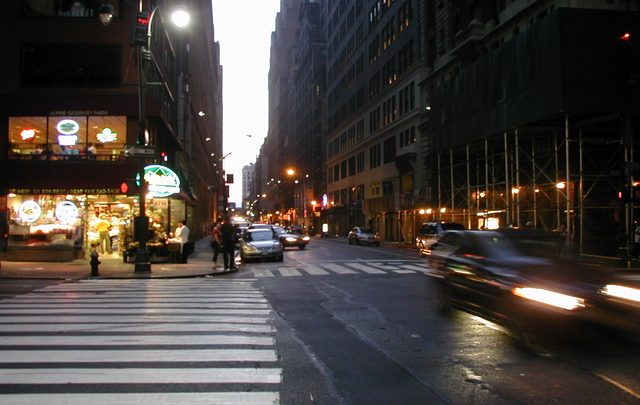 A city street with cars driving down it at night.