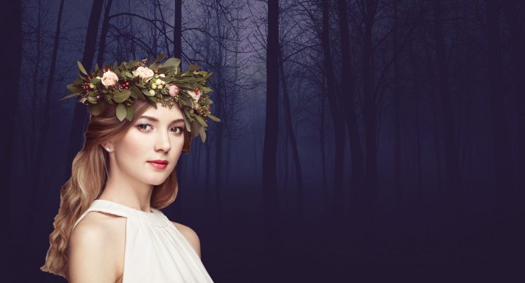 A woman wearing a wreath of flowers in front of trees.
