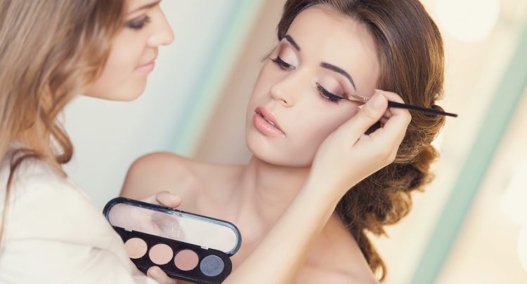 A woman is getting her makeup done by another person.