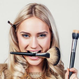 A woman holding two different brushes in her mouth.