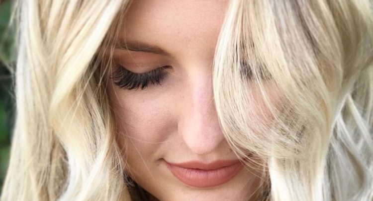 A woman with blonde hair looking down at her face.